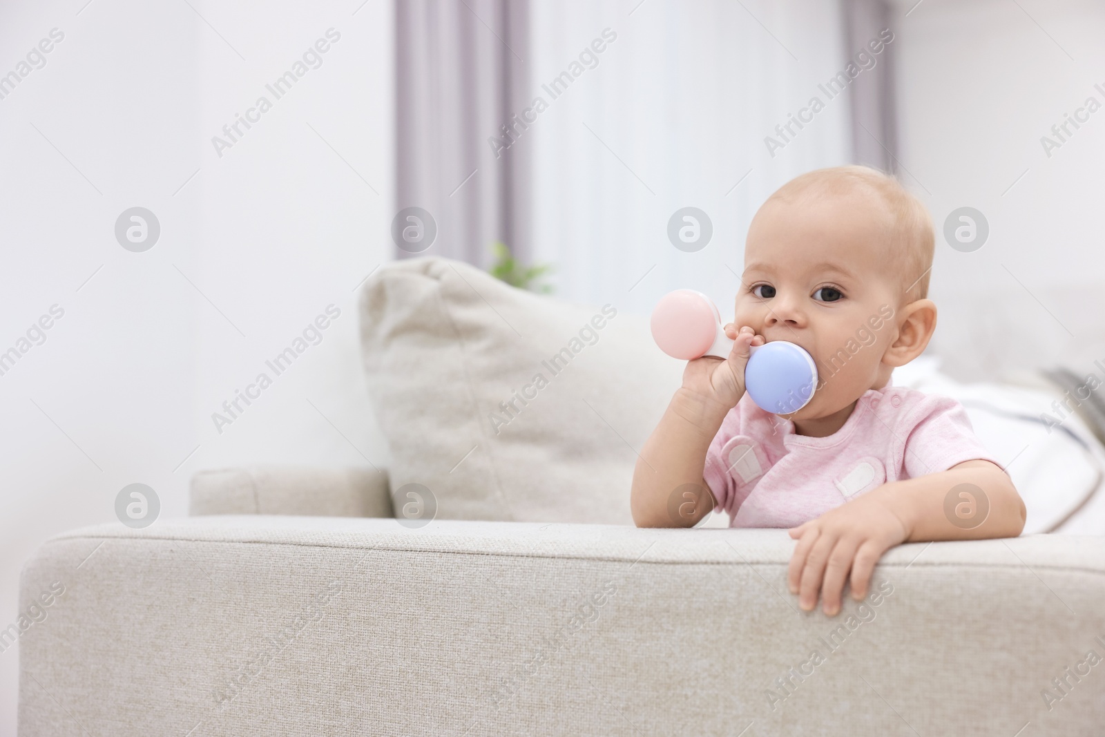 Photo of Cute little baby with rattle on sofa indoors, space for text