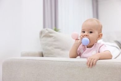 Photo of Cute little baby with rattle on sofa indoors, space for text