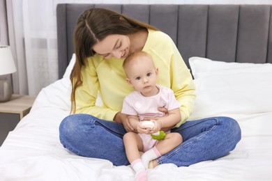 Photo of Mother and her cute little baby with rattle on bed indoors