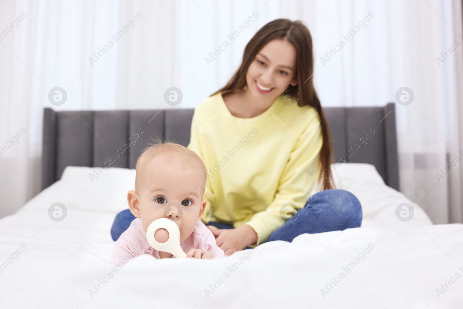 Photo of Mother and her cute little baby with rattle on bed indoors, selective focus