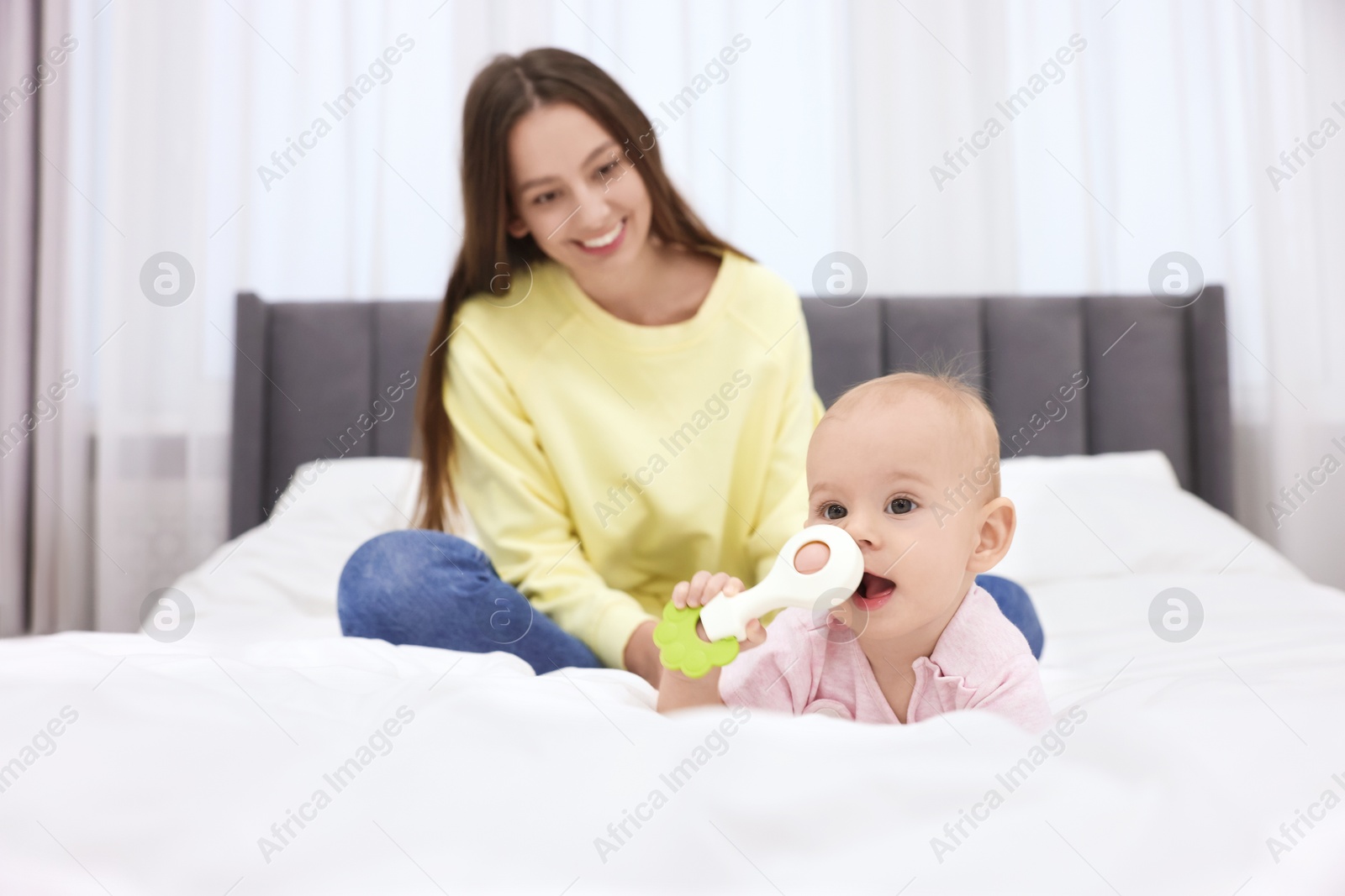 Photo of Mother and her cute little baby with rattle on bed indoors, selective focus