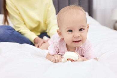 Photo of Mother and her cute little baby with rattle on bed indoors, closeup