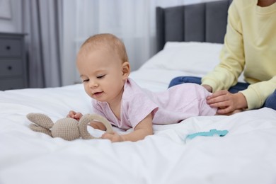 Photo of Mother and her cute little baby with rattles on bed indoors, closeup