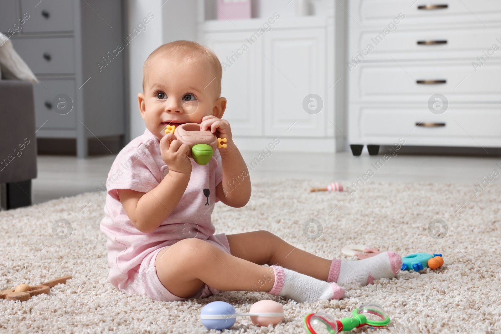 Photo of Cute little baby with rattles on floor indoors, space for text