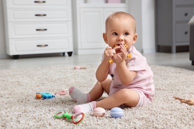 Photo of Cute little baby with rattles on floor indoors, space for text