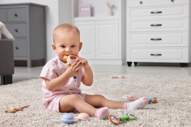 Photo of Cute little baby with rattles on floor indoors, space for text