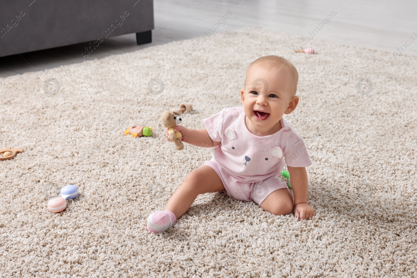 Photo of Cute little baby with rattles on floor indoors