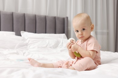 Photo of Cute little baby with rattle on bed indoors