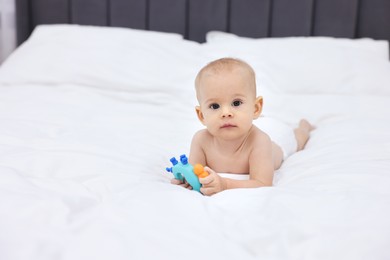 Photo of Cute little baby with rattle on bed indoors, space for text