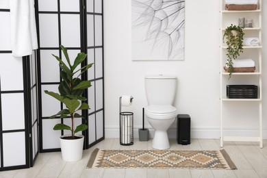 Photo of Stylish restroom interior with folding screen, toilet bowl and houseplant