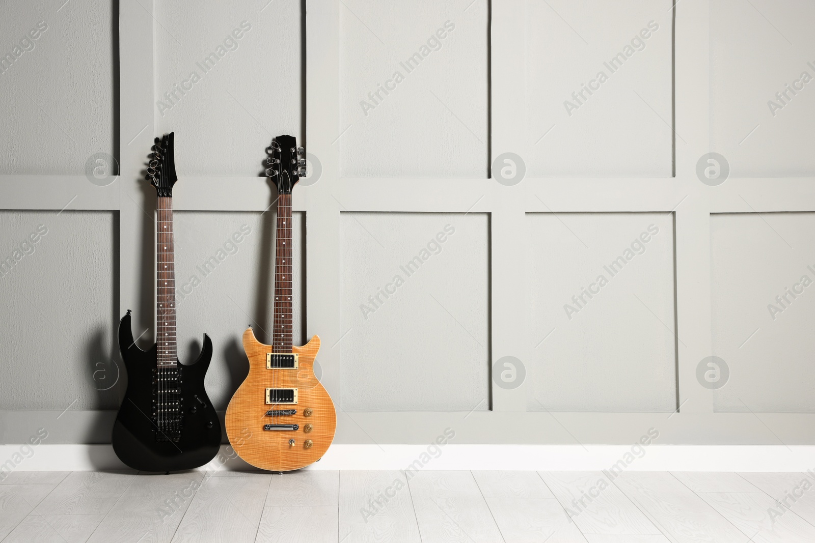 Photo of Two modern electric guitars near grey wall. Space for text