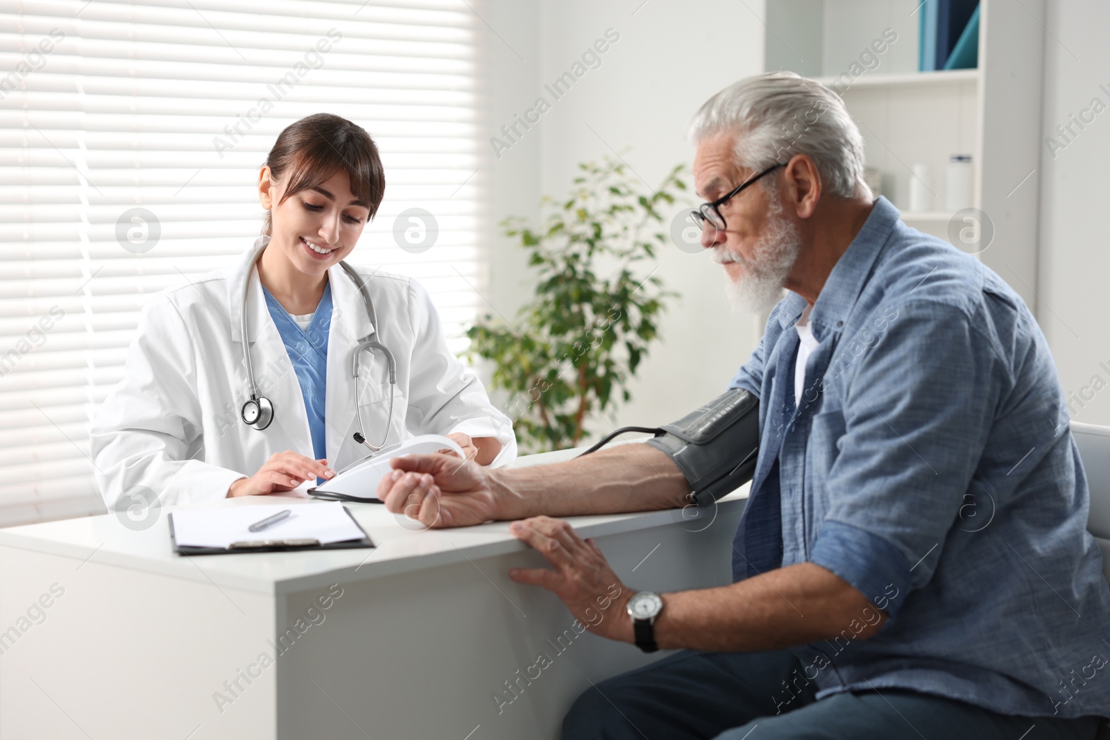 Photo of Doctor measuring senior man's blood pressure during appointment in hospital