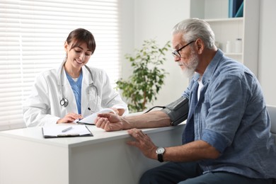 Doctor measuring senior man's blood pressure during appointment in hospital