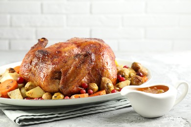 Photo of Delicious baked turkey, vegetables, cranberries and orange sauce on gray textured table against white brick wall