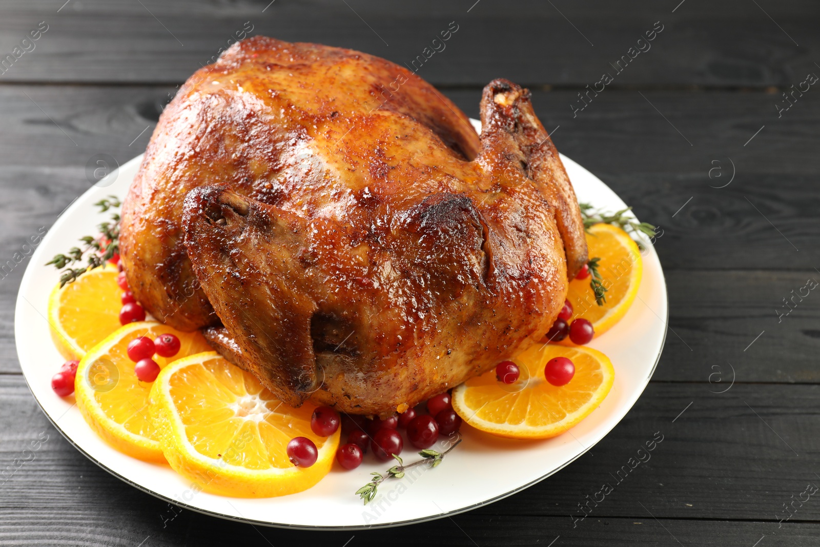 Photo of Delicious baked turkey, orange slices, cranberries and thyme on gray wooden table, closeup