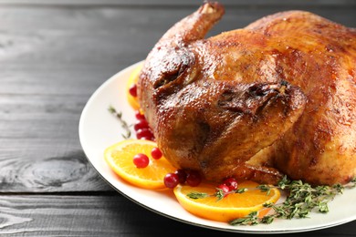 Photo of Delicious baked turkey, orange slices, cranberries and thyme on gray wooden table, closeup