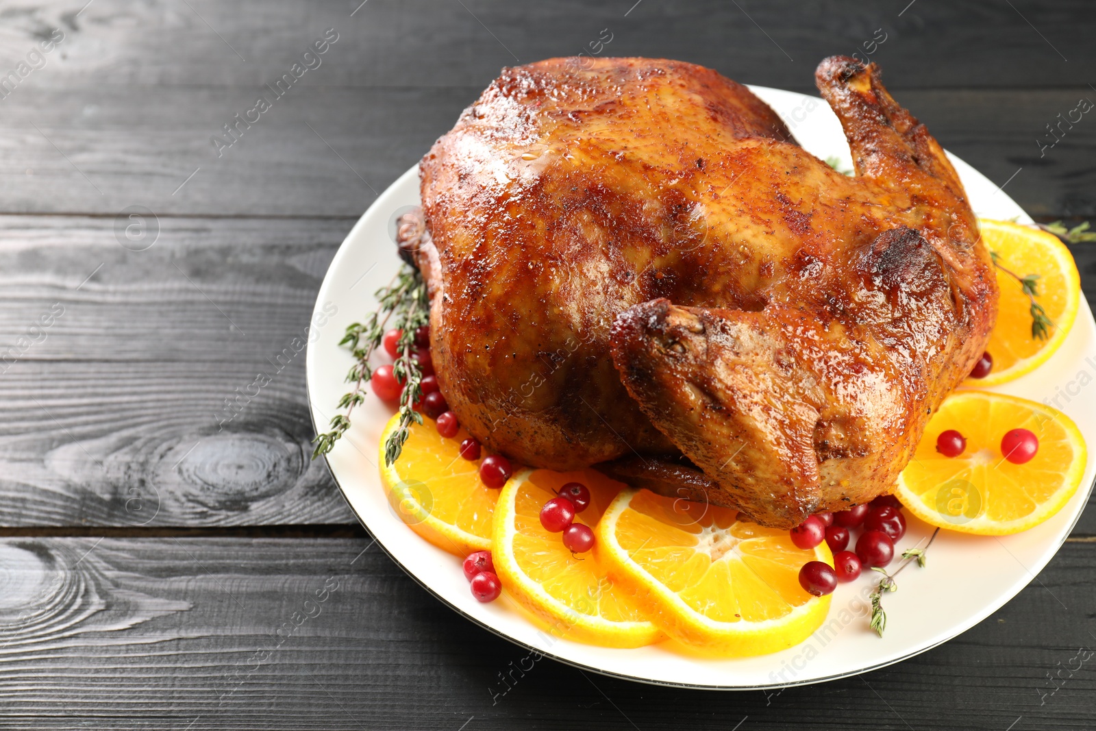 Photo of Delicious baked turkey, orange slices, cranberries and thyme on gray wooden table, closeup. Space for text