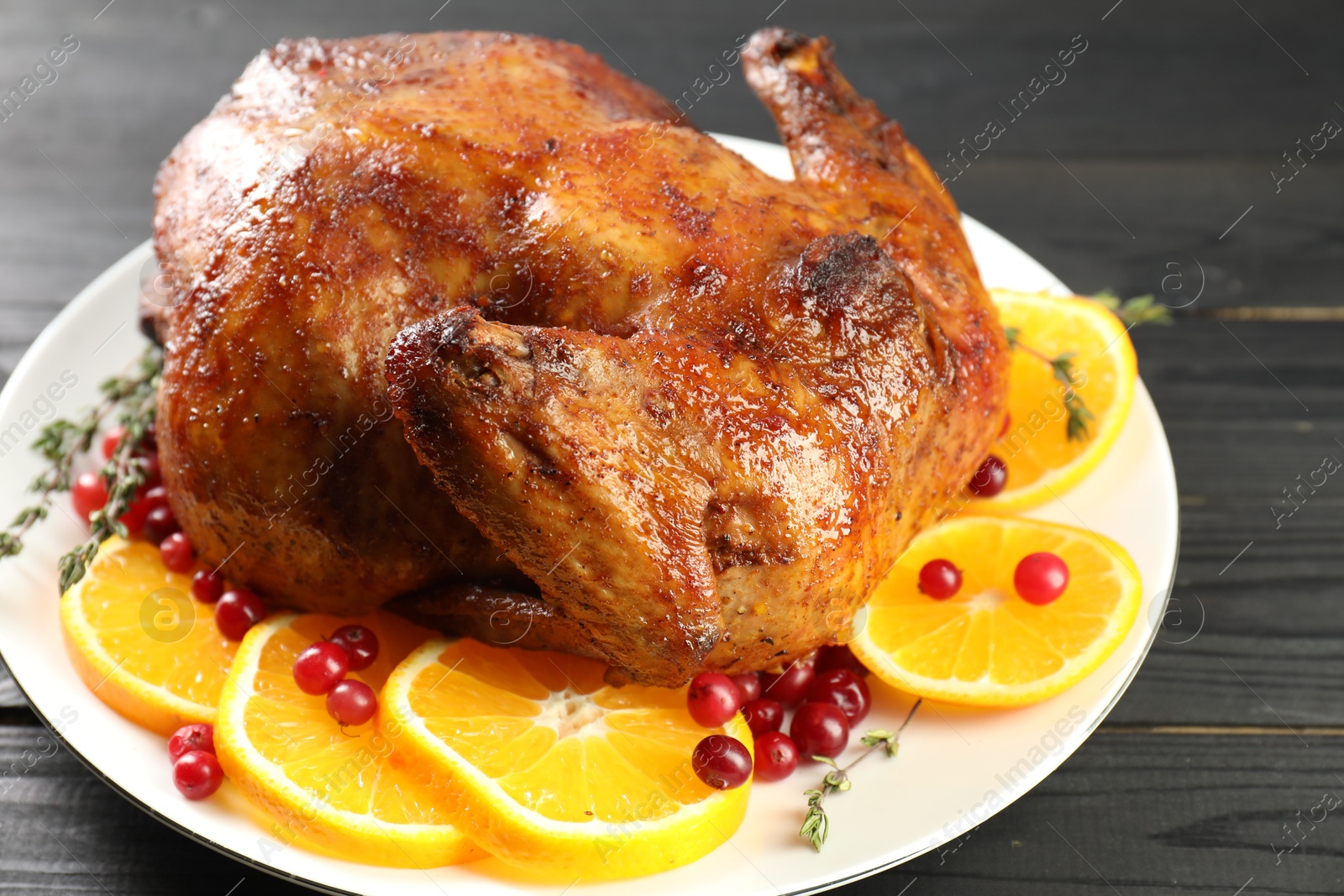 Photo of Delicious baked turkey, orange slices, cranberries and thyme on gray wooden table, closeup