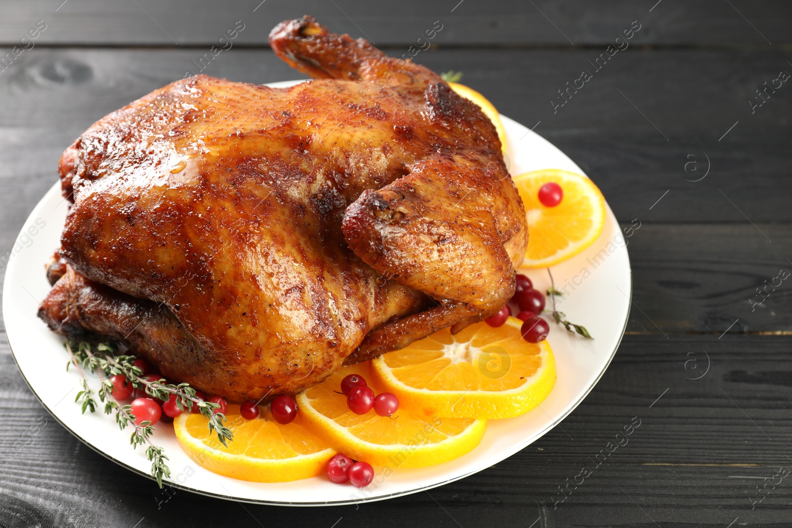 Photo of Delicious baked turkey, orange slices, cranberries and thyme on gray wooden table, closeup