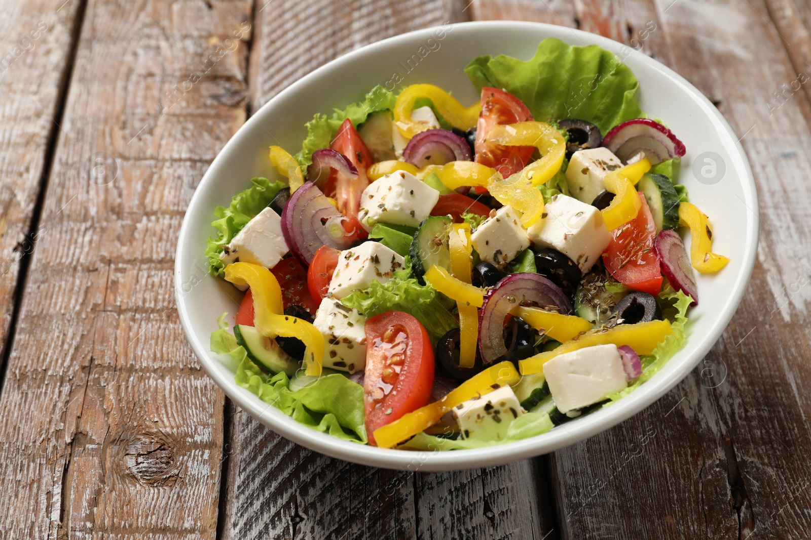 Photo of Delicious fresh Greek salad in bowl on wooden table, closeup