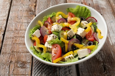 Photo of Delicious fresh Greek salad in bowl on wooden table, closeup