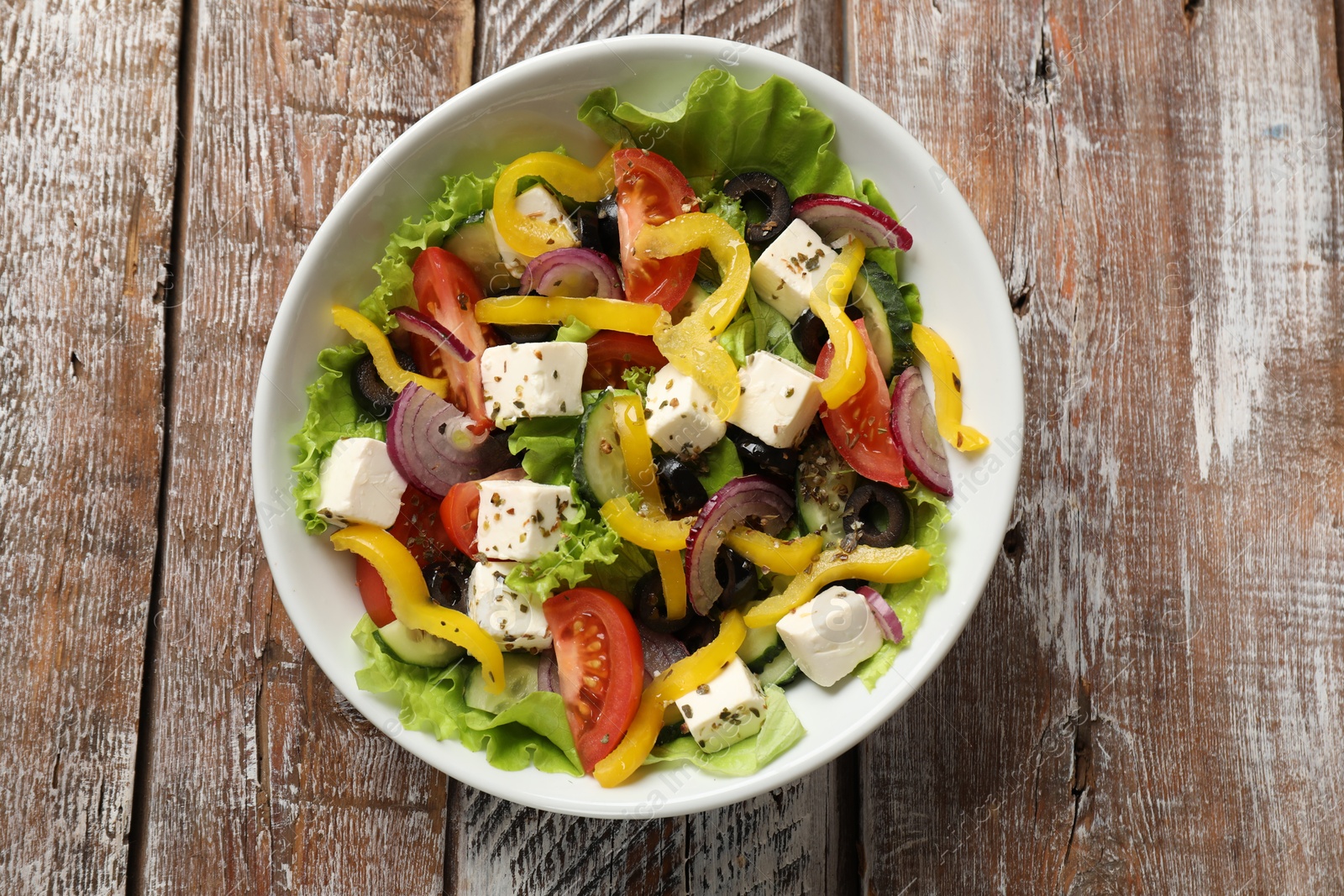 Photo of Delicious fresh Greek salad in bowl on wooden table, top view