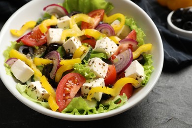 Photo of Delicious fresh Greek salad in bowl on black table, closeup