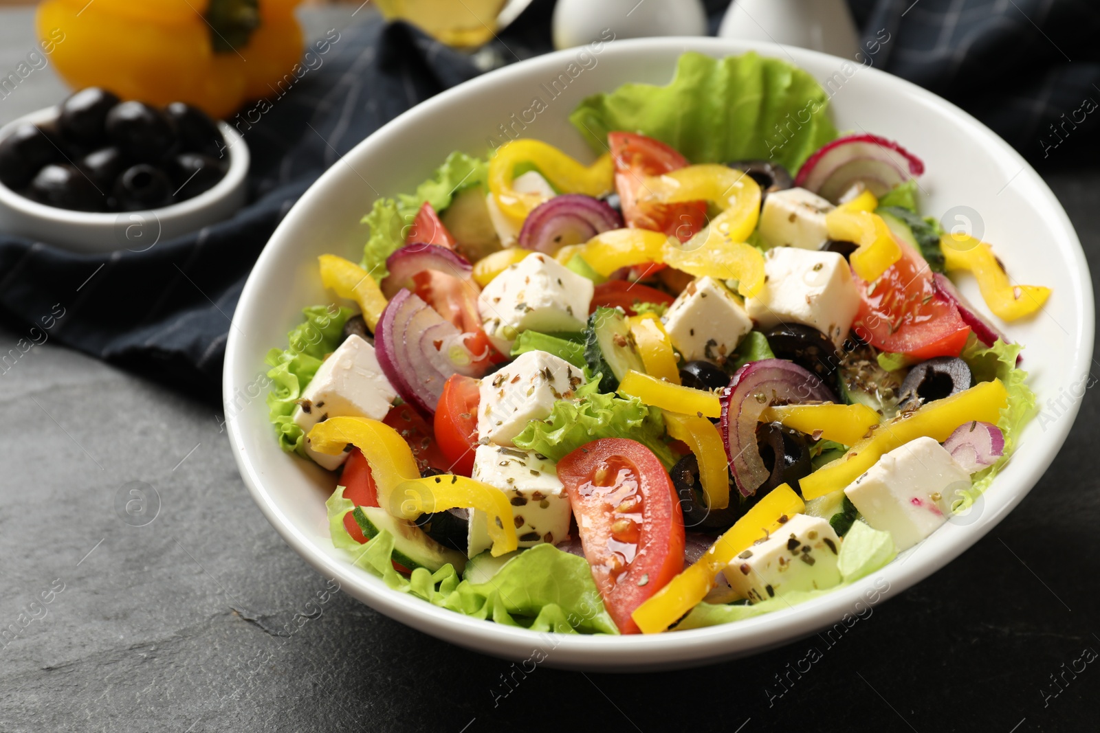 Photo of Delicious fresh Greek salad in bowl on black table, closeup