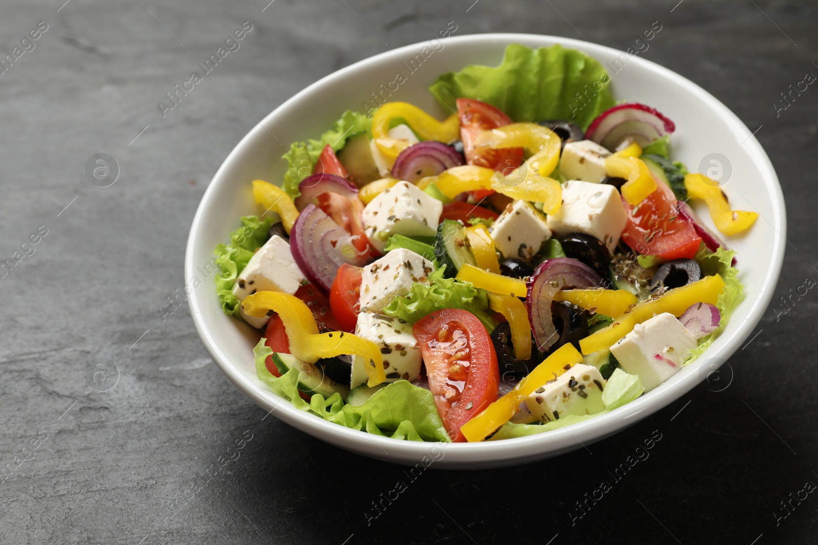 Photo of Delicious fresh Greek salad in bowl on black table, closeup