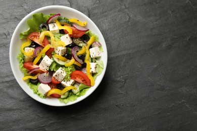 Photo of Delicious fresh Greek salad in bowl on black table, top view. Space for text