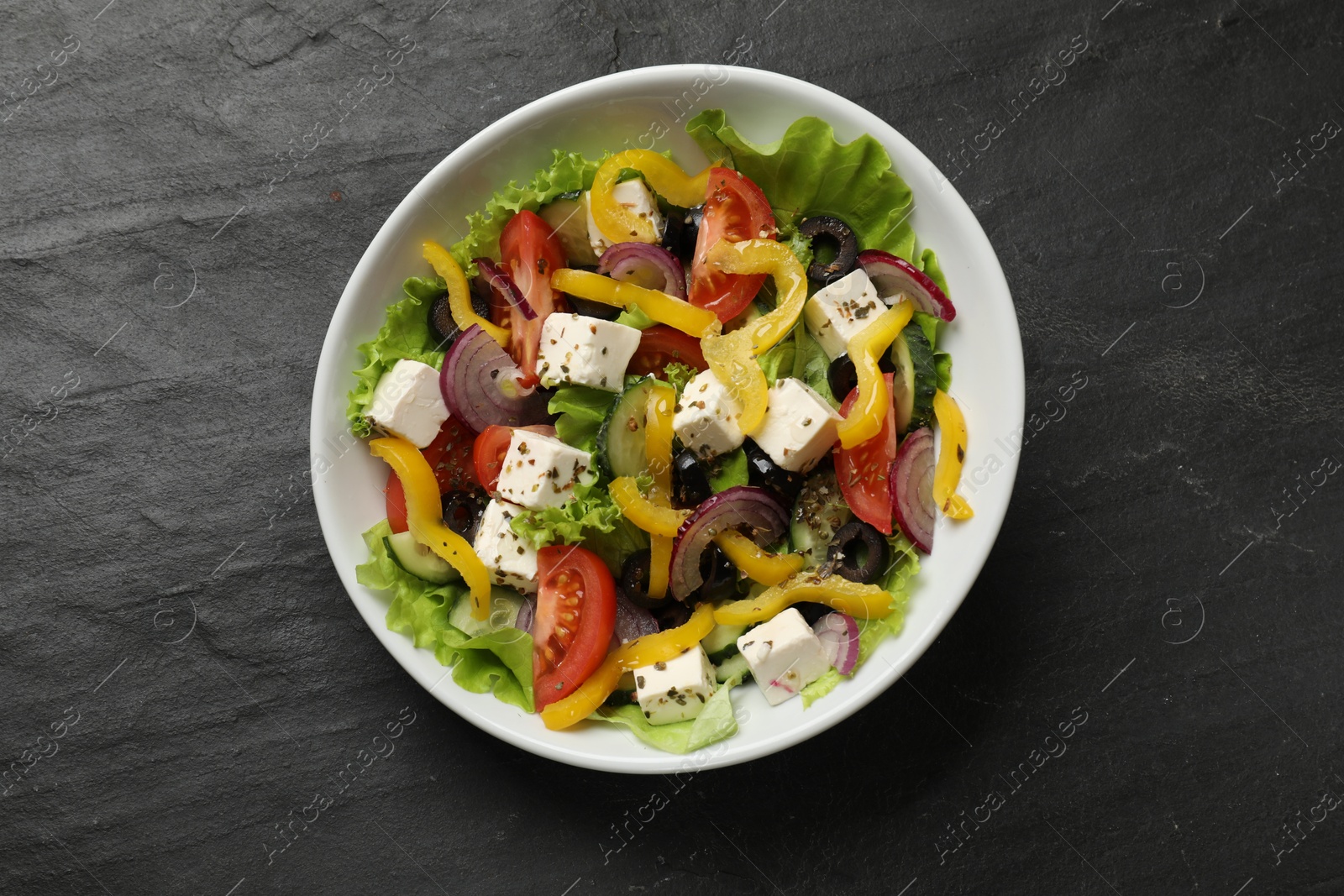 Photo of Delicious fresh Greek salad in bowl on black table, top view