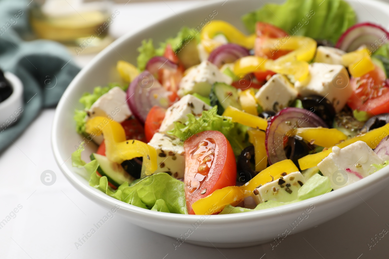 Photo of Delicious fresh Greek salad in bowl on white table, closeup