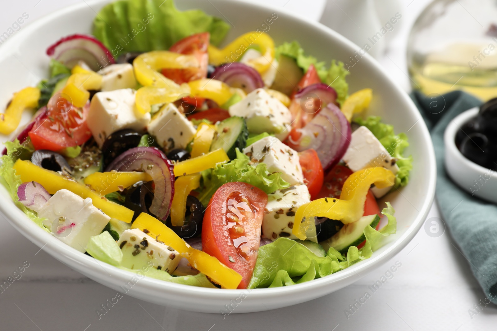 Photo of Delicious fresh Greek salad in bowl on white table, closeup