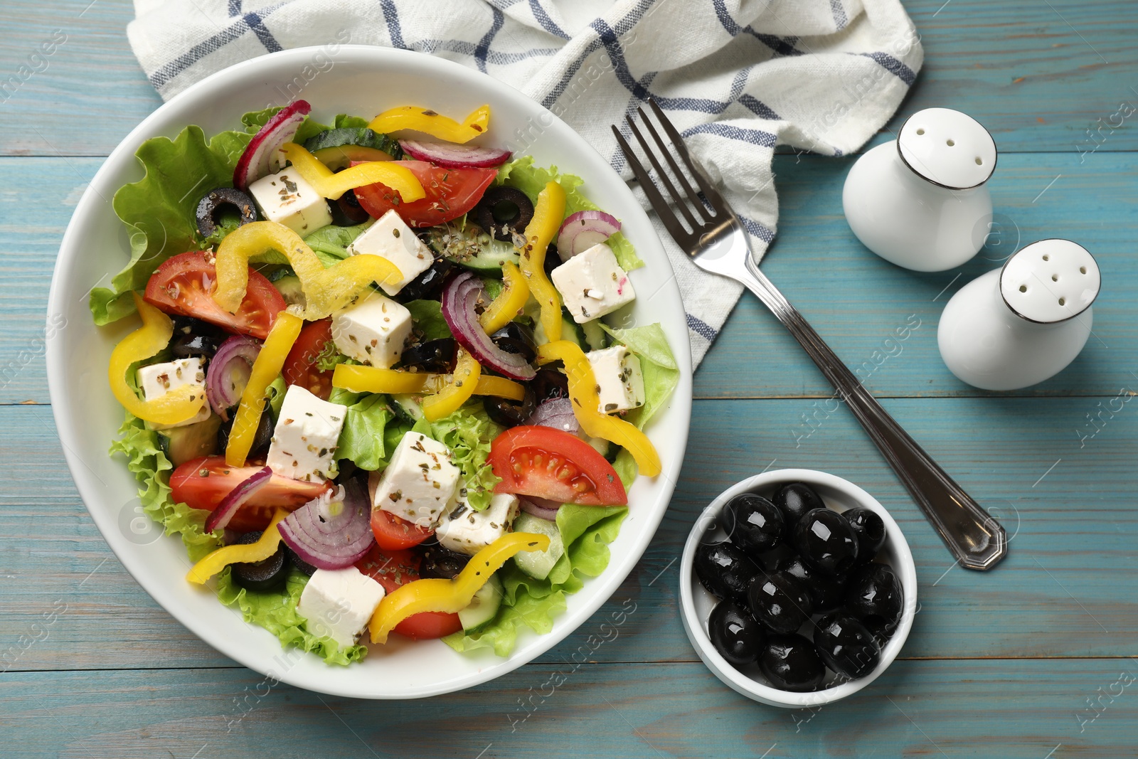 Photo of Delicious fresh Greek salad served on light blue wooden table, flat lay