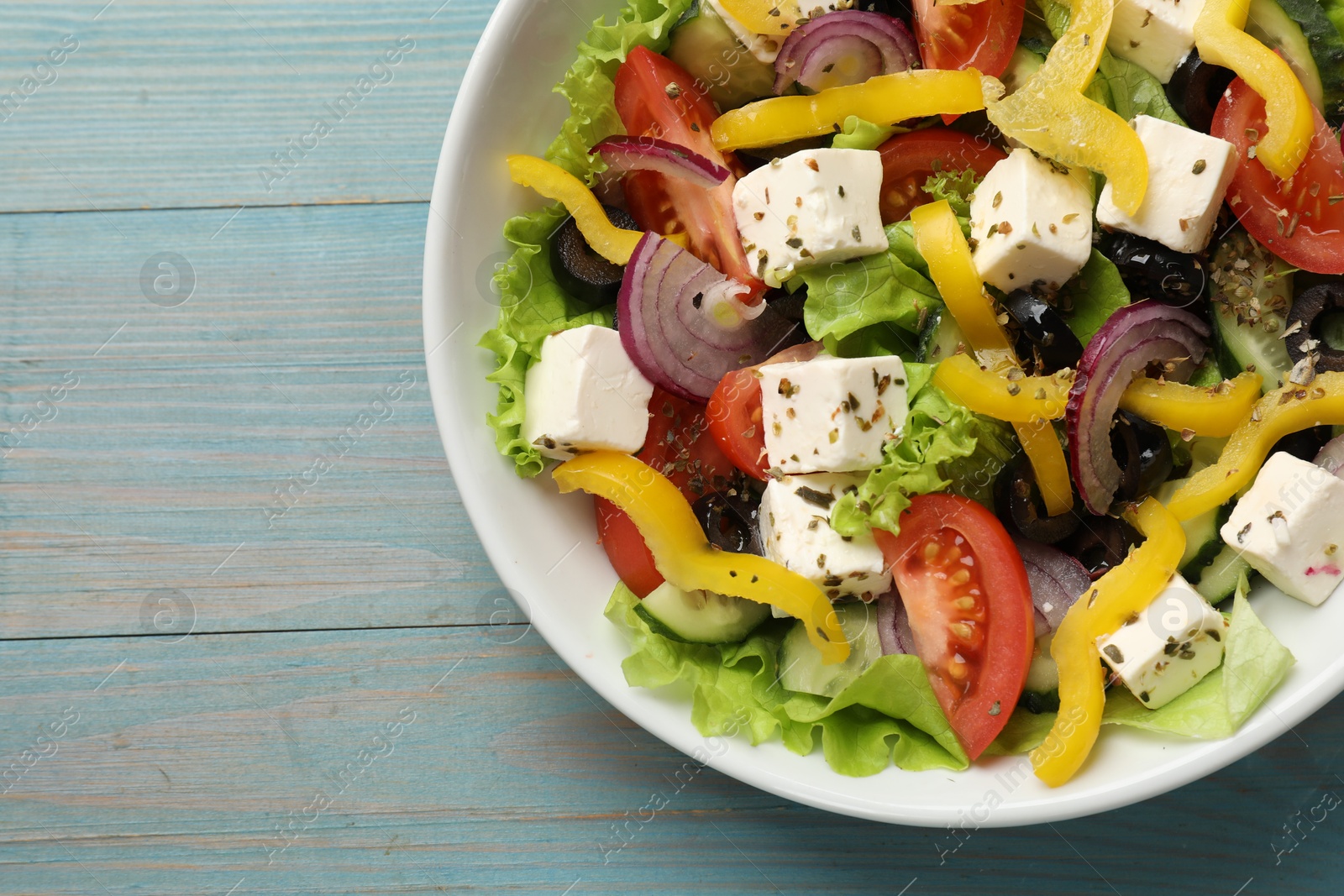 Photo of Delicious fresh Greek salad on light blue wooden table, top view. Space for text