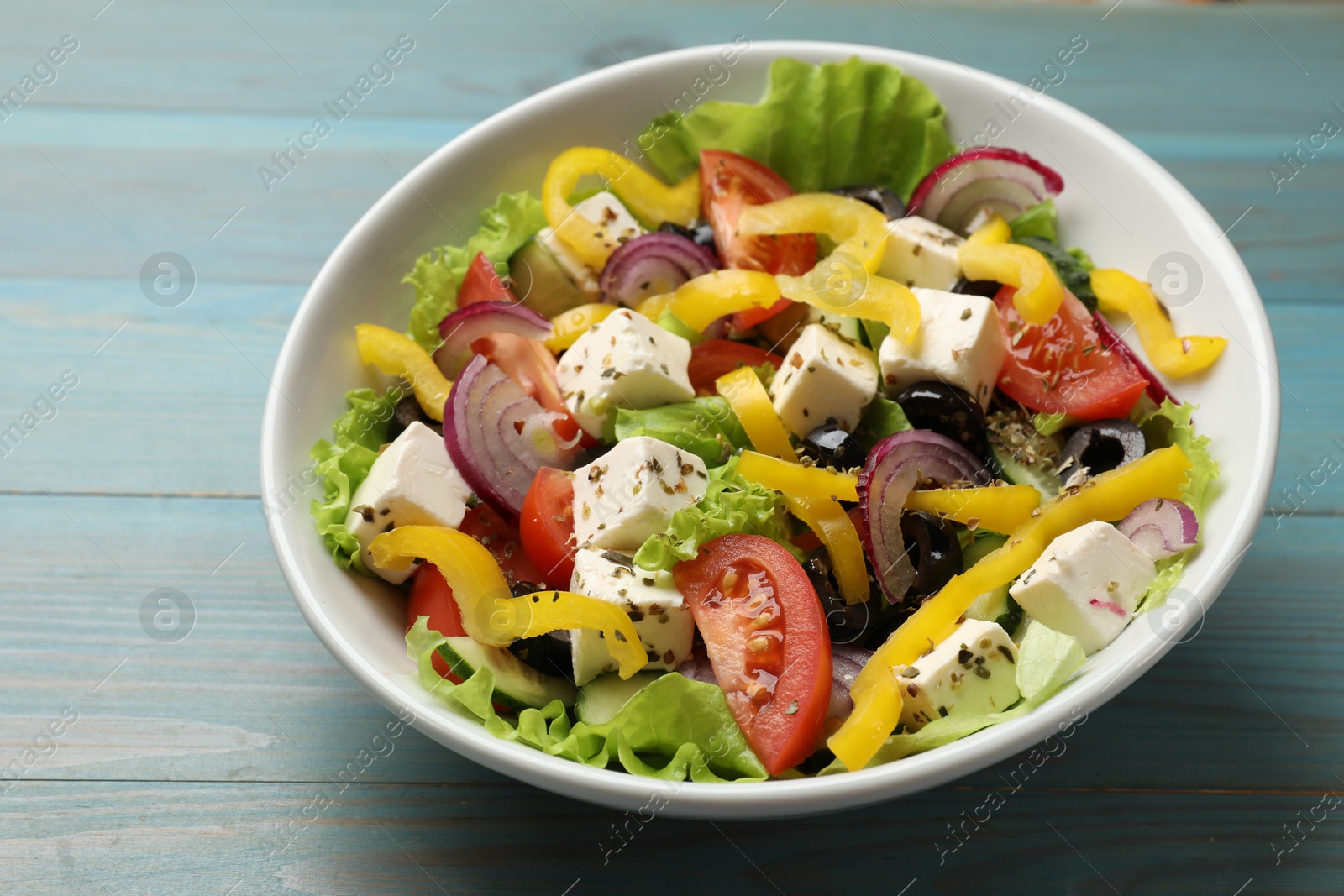 Photo of Delicious fresh Greek salad in bowl on light blue wooden table, closeup