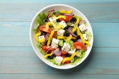 Photo of Delicious fresh Greek salad in bowl on light blue wooden table, top view