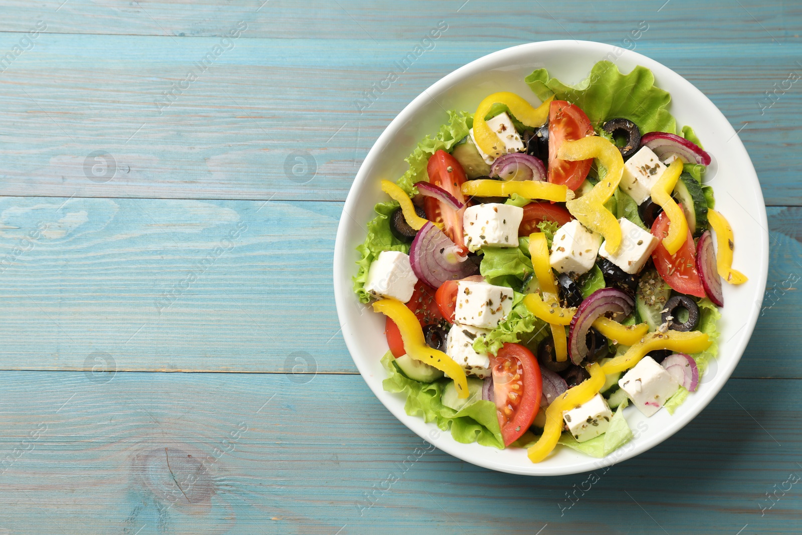 Photo of Delicious fresh Greek salad in bowl on light blue wooden table, top view. Space for text