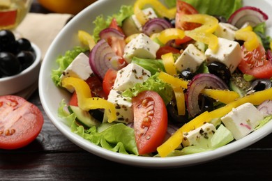 Photo of Delicious fresh Greek salad in bowl on wooden table, closeup