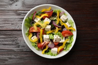 Photo of Delicious fresh Greek salad in bowl on wooden table, top view