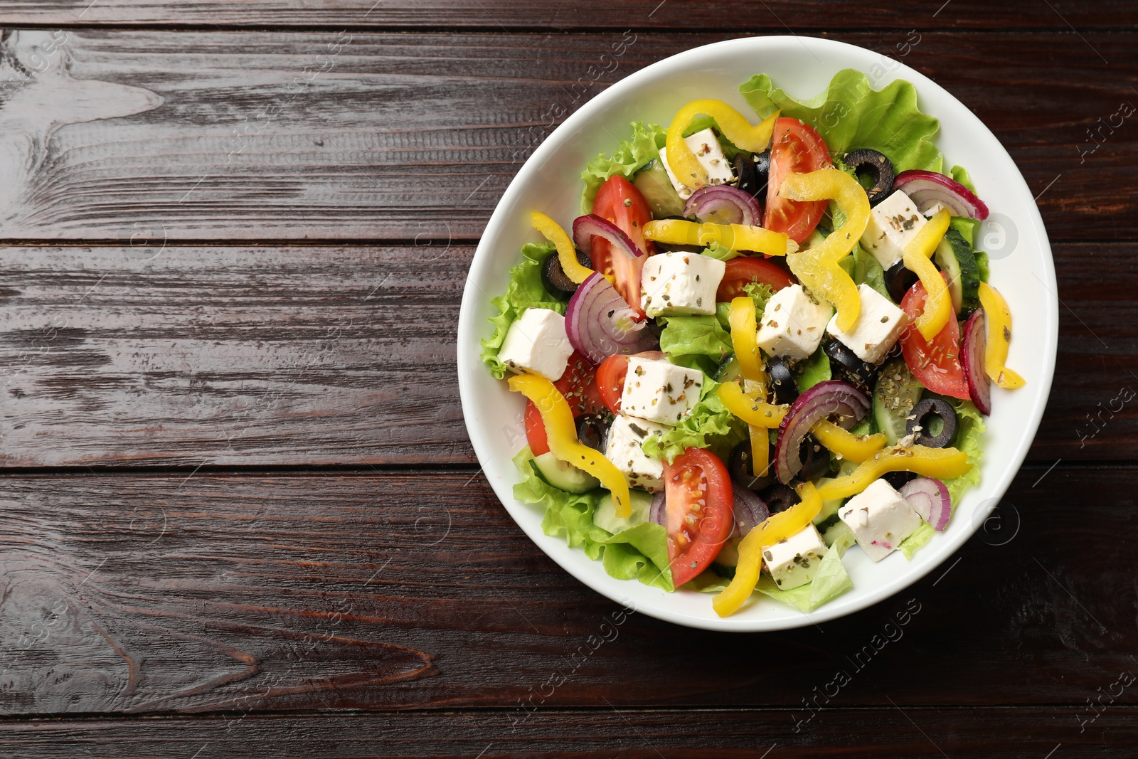 Photo of Delicious fresh Greek salad in bowl on wooden table, top view. Space for text