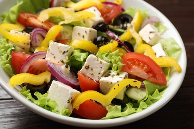 Photo of Delicious fresh Greek salad in bowl on wooden table, closeup