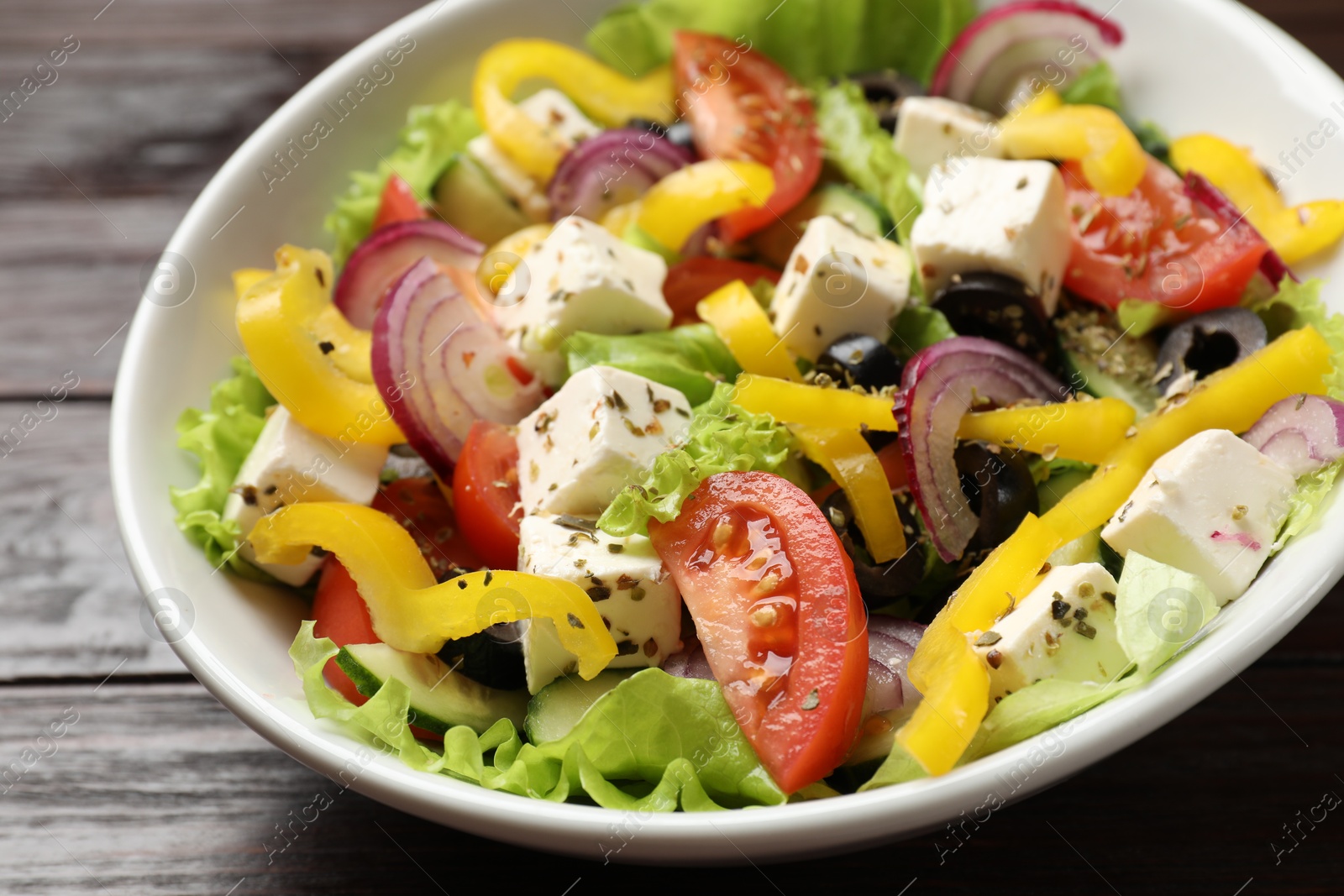 Photo of Delicious fresh Greek salad in bowl on wooden table, closeup