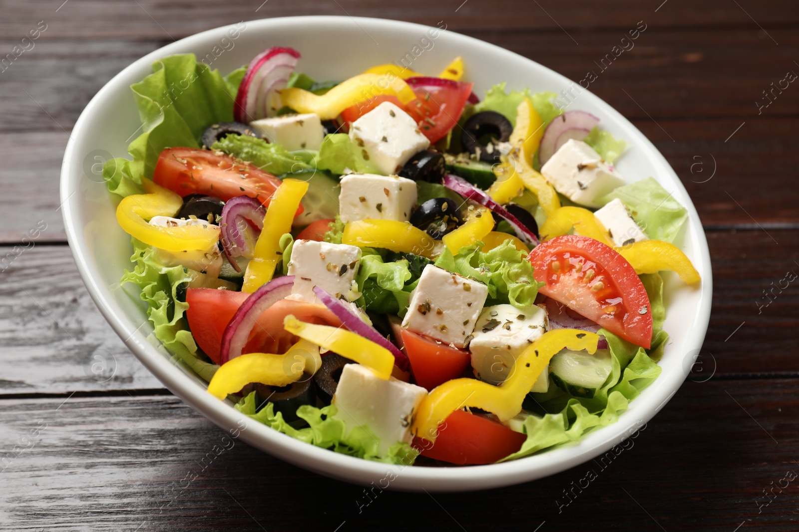 Photo of Delicious fresh Greek salad in bowl on wooden table, closeup