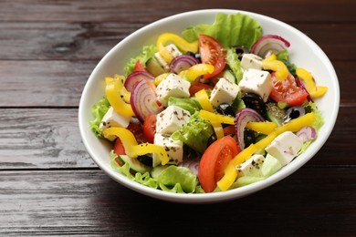 Photo of Delicious fresh Greek salad in bowl on wooden table, closeup