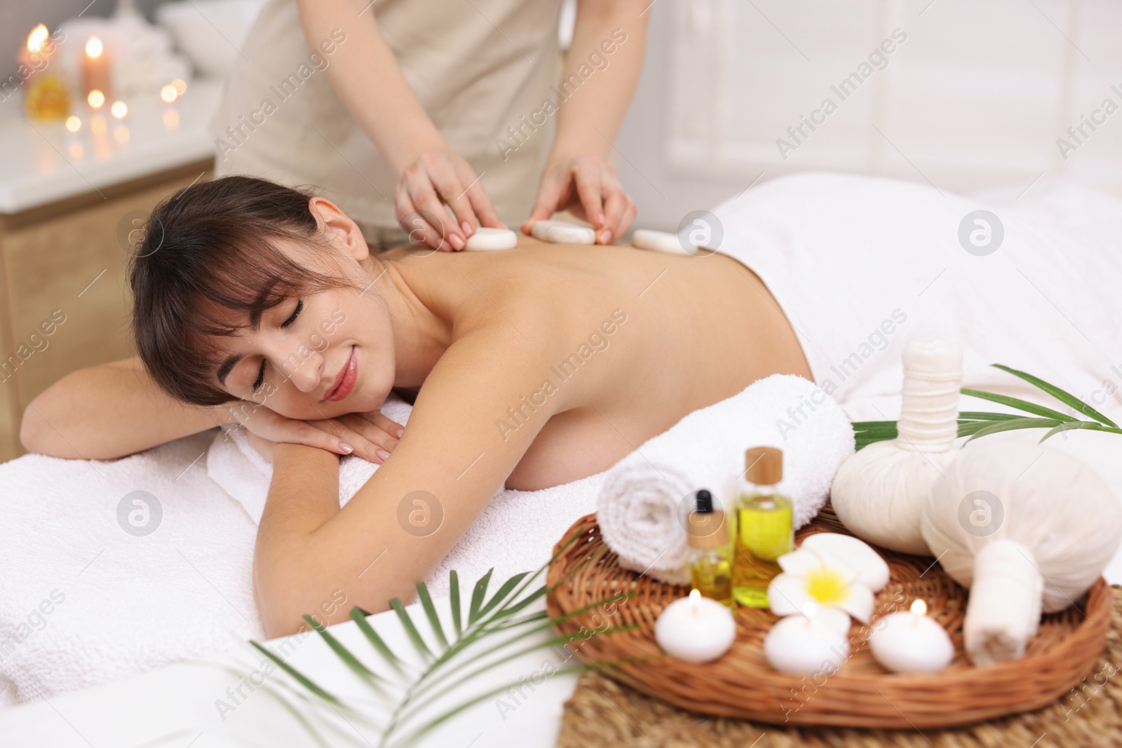 Photo of Young woman receiving hot stone massage in spa salon