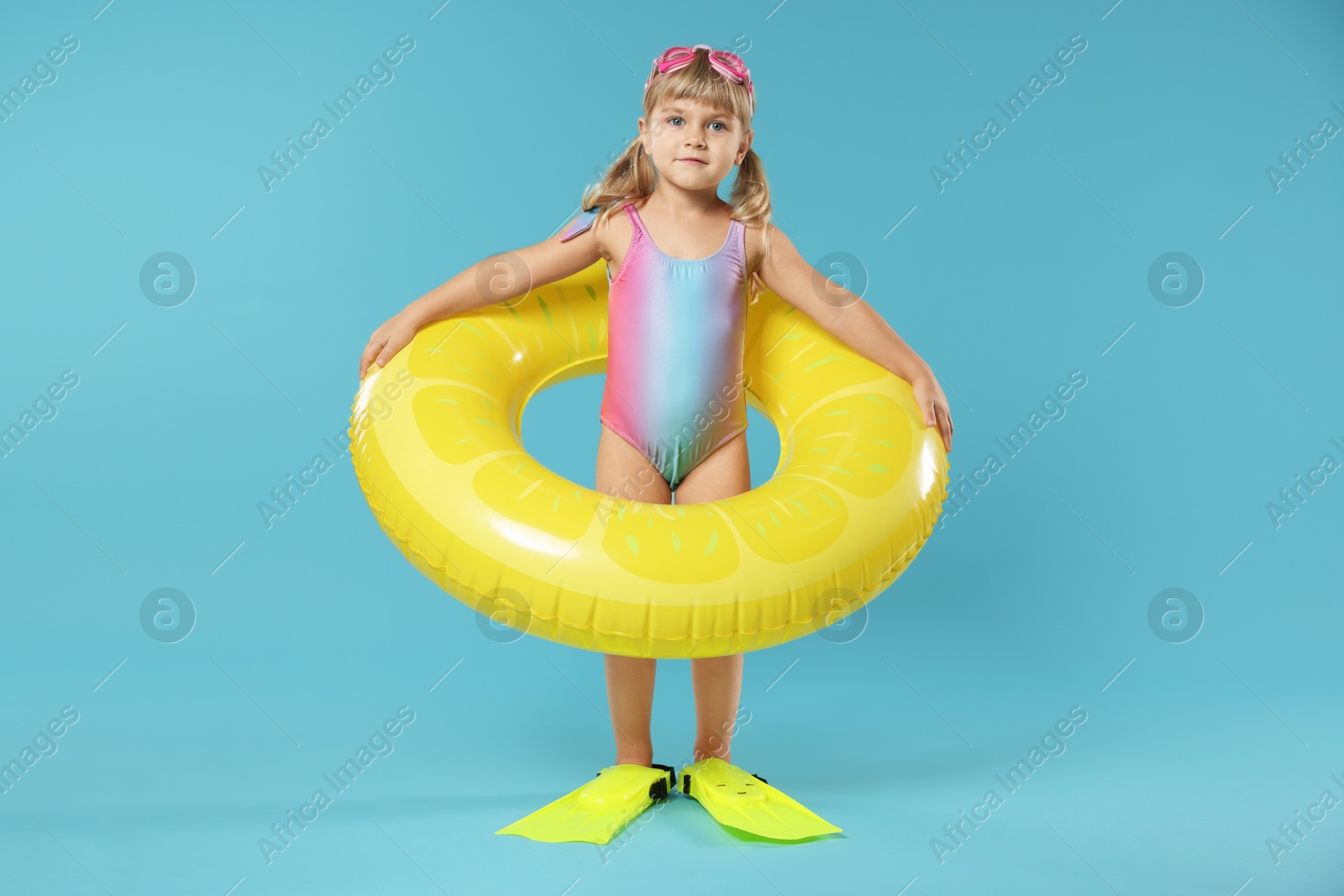 Photo of Cute little girl in beachwear with diving mask, inflatable ring and flippers on light blue background