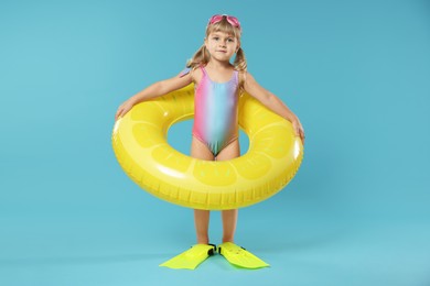 Photo of Cute little girl in beachwear with diving mask, inflatable ring and flippers on light blue background