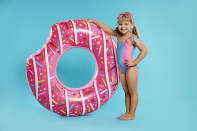 Photo of Cute little girl in beachwear with diving mask and inflatable ring on light blue background