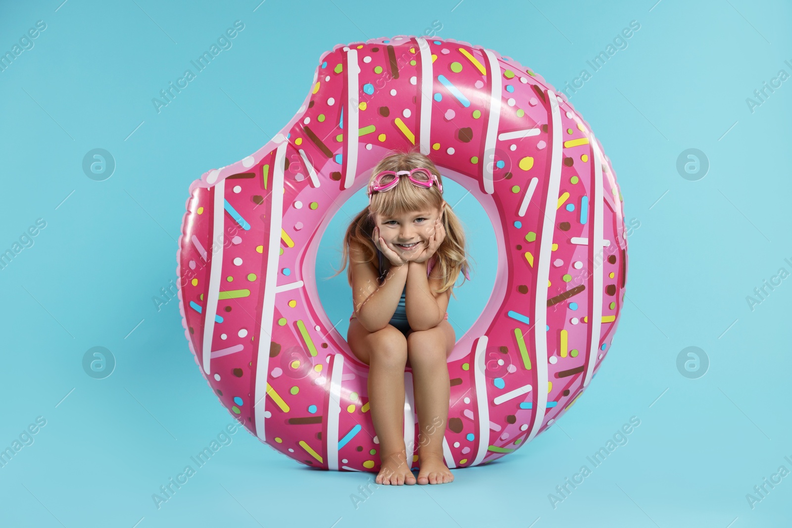 Photo of Cute little girl in beachwear with diving mask and inflatable ring on light blue background